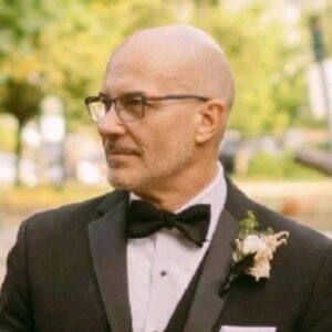 Joe Sikora in a black tuxedo and bow tie outdoors at an event.
